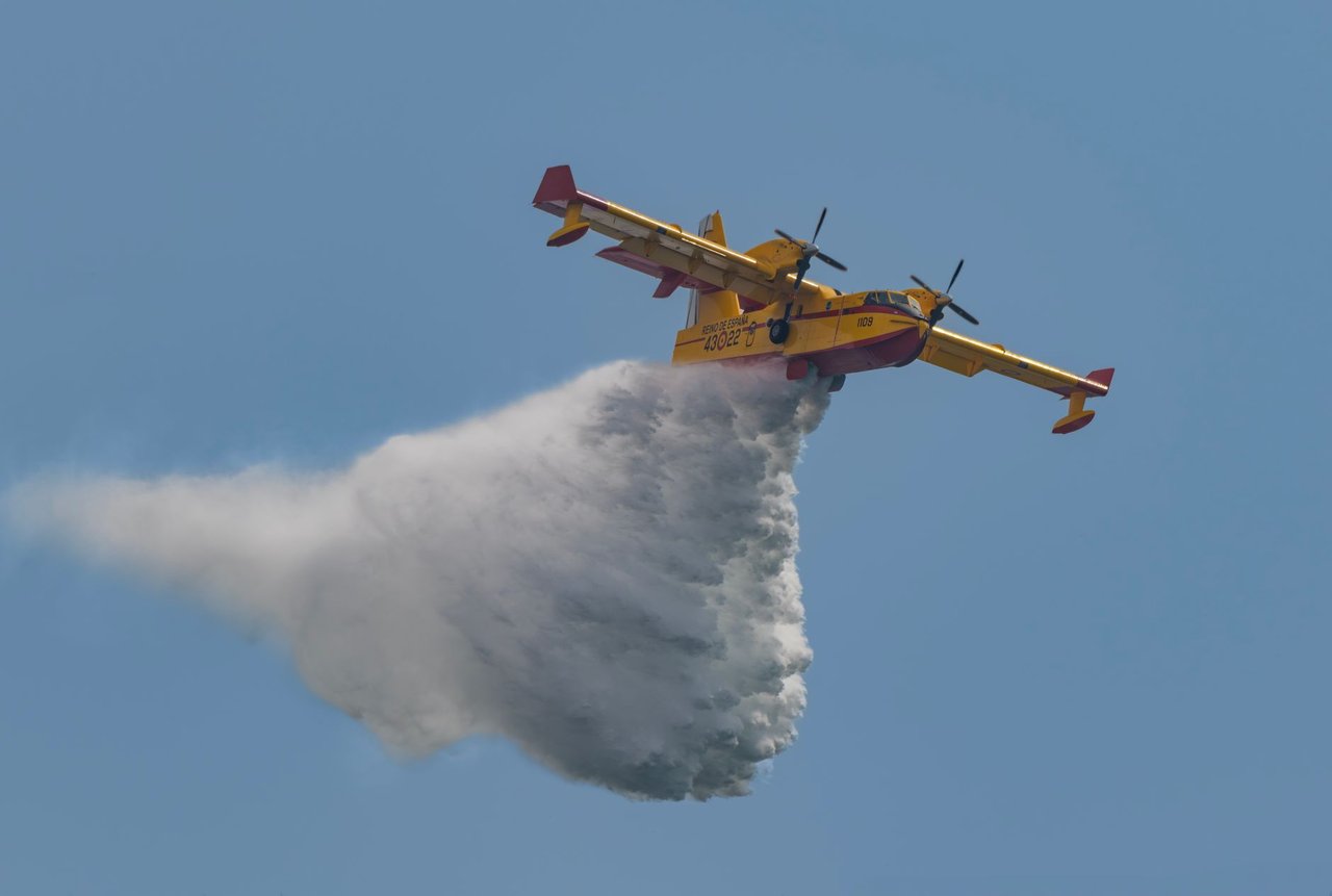 Avião de combate a incêndios despeja água sobre uma área em chamas durante uma operação de emergência.