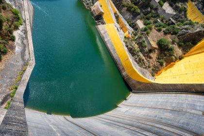Vista aérea de uma grande barragem hidrelétrica, com água represada e estruturas de concreto.