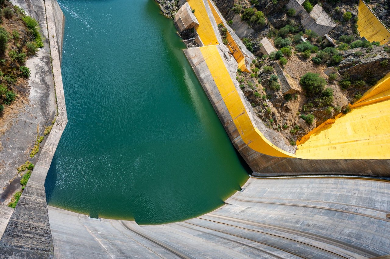 Vista aérea de uma grande barragem hidrelétrica, com água represada e estruturas de concreto.