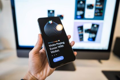 Mão segurando um smartphone com um aplicativo de carteira digital exibido na tela, em ambiente interno.