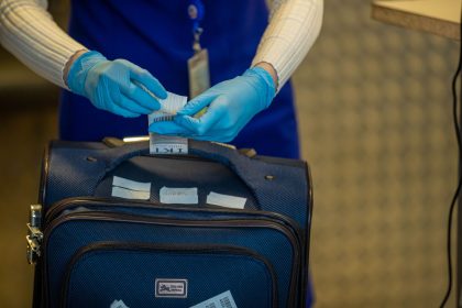 Mãos protegidas por luvas inspecionam etiquetas de bagagem durante um procedimento de segurança em aeroporto.