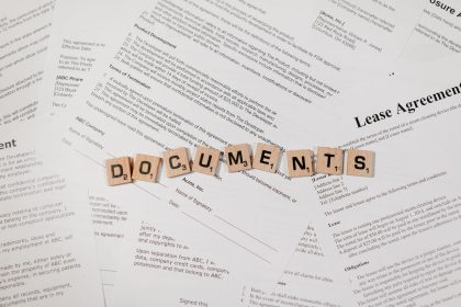 Peças de jogo formam a palavra “DOCUMENTS” sobre documentos e contratos dispostos em uma mesa.